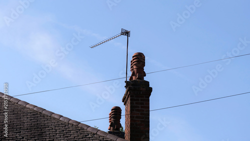 Foto Television antenna on brick chimney stack, traditional house roof against clear
