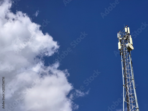 Fotografía Cellular communication tower with antennas against blue sky and white clouds, wi