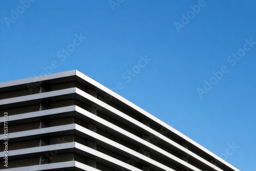 Abstract geometric facade of modern corporate office building against clear blue sky. Minimalist architectural background with generous copy space for business or real estate concept.