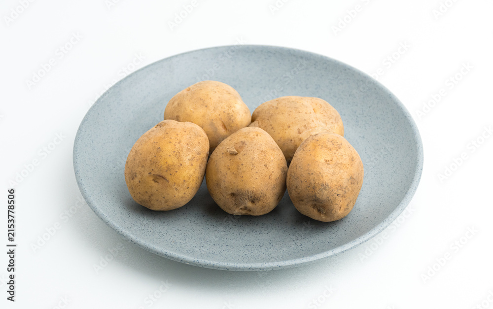 Fototapeta premium Fresh raw baby potatoes served on a grey ceramic plate isolated on white background