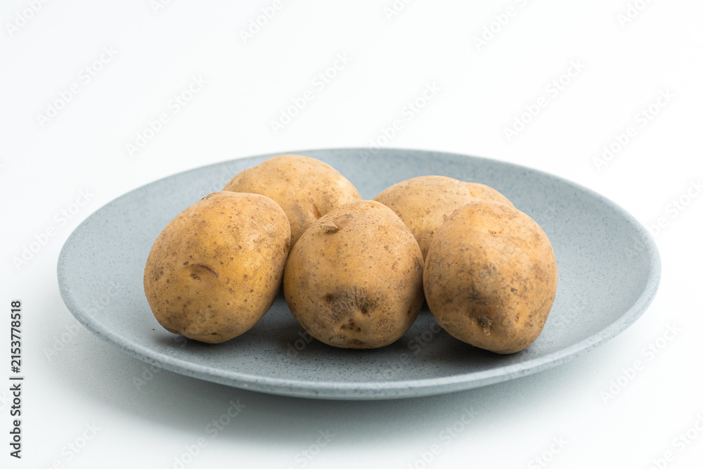 Fototapeta premium Fresh raw baby potatoes served on a grey ceramic plate isolated on white background