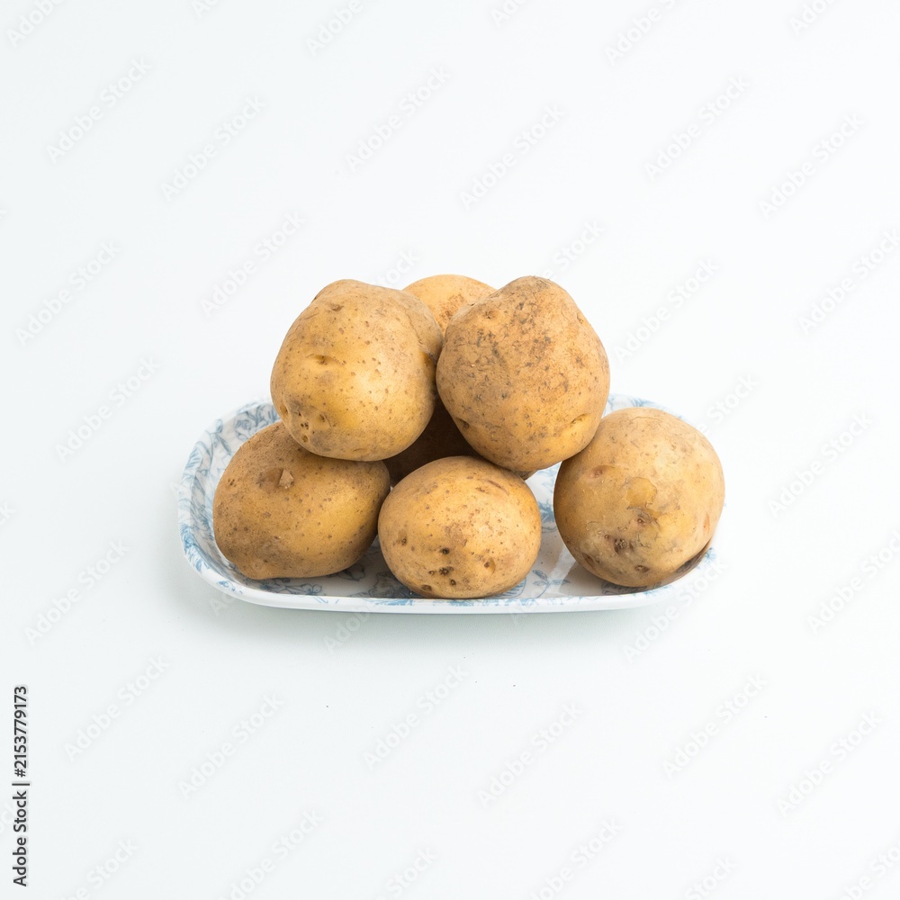 Fototapeta premium Fresh raw brown potatoes served on a blue patterned ceramic plate isolated on white background