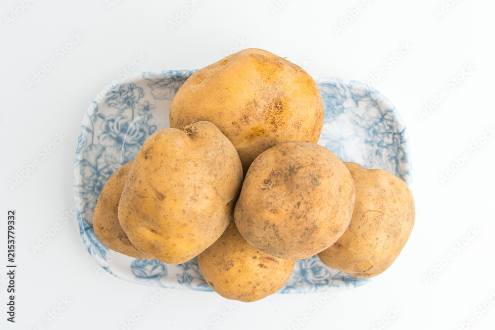Fototapeta premium Fresh raw brown potatoes served on a blue patterned ceramic plate isolated on white background