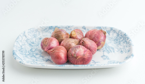 Fotografía Fresh red onions shallots served on a blue patterned ceramic plate isolated on w