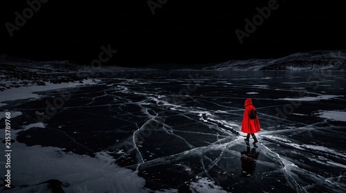 Hooded figure in red coat walks across cracked frozen lake during dark arctic winter night.
