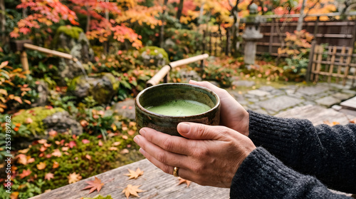 Person holding a cup of matcha tea in a Japanese garden during autumn
