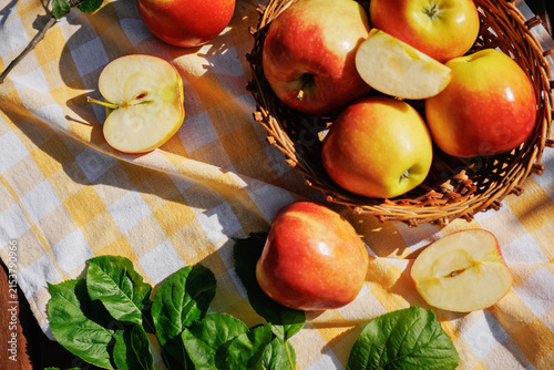 Fotografía Fresh red and yellow apples in a wicker basket with sliced apples on a checkered