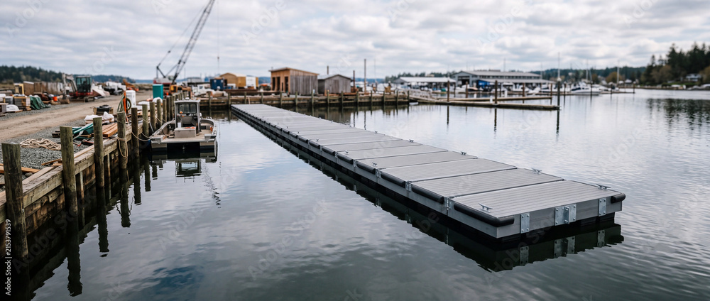 Obraz premium Floating dock and marina pier at a quiet harbor with overcast sky and waterfront buildings