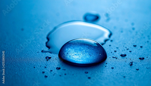 Macro photography of water droplets on blue textured surface. Abstract ultra-macro of a single large spherical water droplet with dynamic internal light reflections, surrounded by smaller splashes.