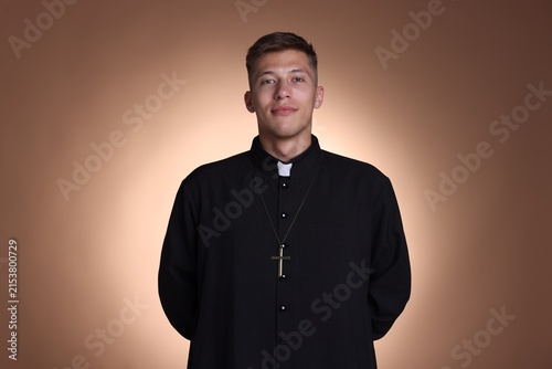 Obraz na plátně Portrait of young priest in cassock on beige background