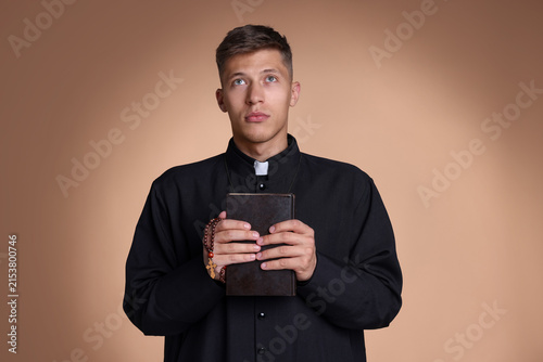 Fotografie Priest with rosary and Holy Bible praying on beige background