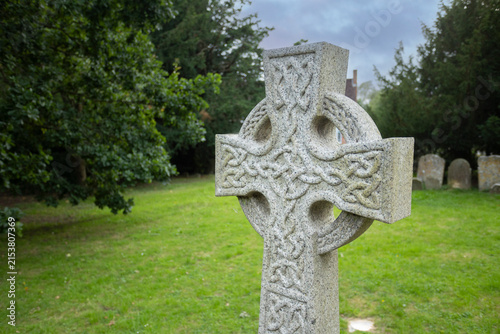 Foto Granite Celtic cross headstone standing in a green churchyard cemetery, featuring intricate carved knotwork