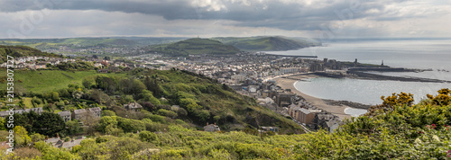 Panoramic View Of A Aberystwyth Coastal Town, Bay and Green Hills Under a Cloudy Sky