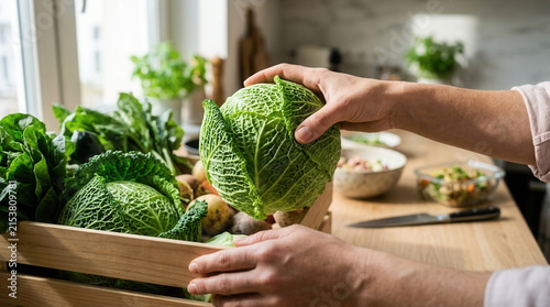 Fresh Cabbage Being Held Above Wooden Crate of Vegetables