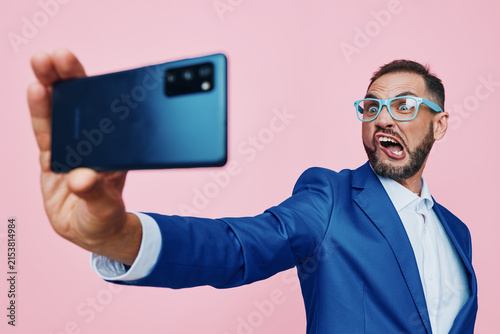A professional man in a blue suit takes a confident selfie against a vibrant pink backdrop, conveying ambition, style, and a dynamic, forward looking business mood.