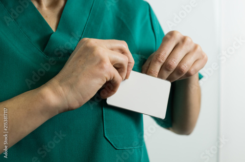 Midsection shot of a medical professional wearing green scrubs holding a blank white name tag card with both hands.