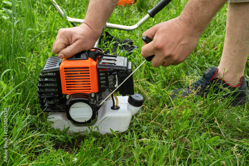 In a grassy area, a person pulls the starter cord of a small engine attached to a lawn mower. The sun is out and the grass is lush. The task is to start mowing the lawn