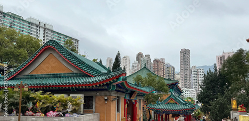 serene chinese temple in urban area with high-rise buildings in the background, wide-angle shot from ground level, ceramic tiles, brick walls, wooden beams, green and brown tones, cultural.