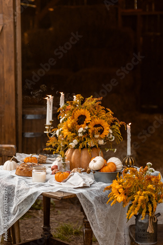 Cozy autumn composition near old wooden country house. Table setting for family thanksgiving dinner with homemade apple pie, bouquet of sunflowers, pumpkins. Elegant rustic cottage core home decor