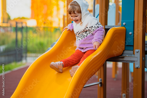 Happy little girl sliding down a playground slide at an outdoor park. Childhood fun, active play, recreation, and joyful summer adventure concept.