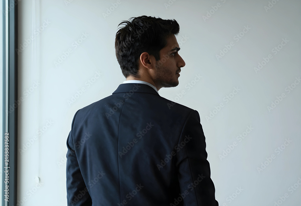 Obraz premium Young businessman in a dark suit looking out a window, contemplating future business strategies and career growth