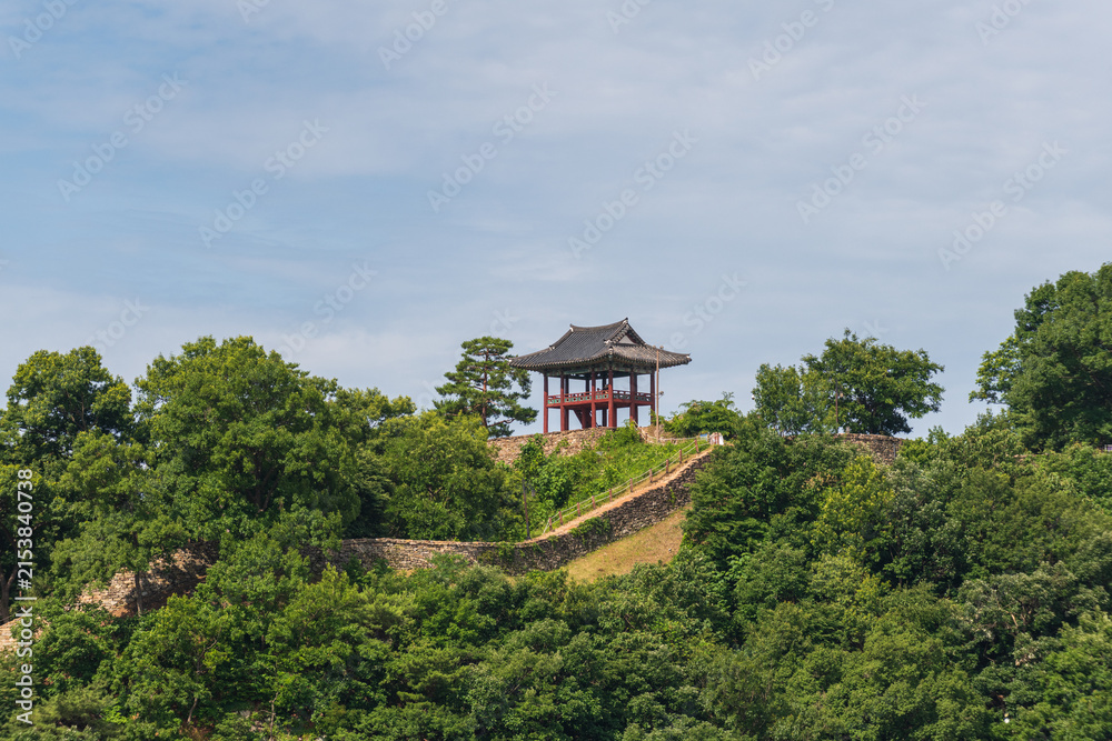 Fototapeta premium Traditional Korean pavilion above a historic stone fortress wall surrounded by lush summer forest in South Korea.