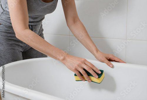 Woman cleaning a white bath...