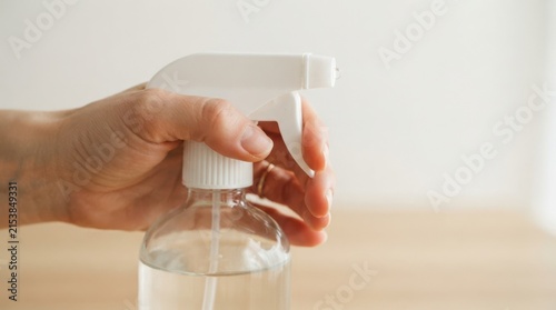 Woman holding a clear glass spray bottle with liquid for cleaning and disinfecting surfaces