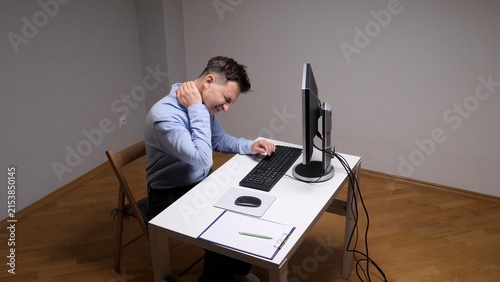 Obraz na plátně Man experiencing acute neck and shoulder pain while working at a computer in a h
