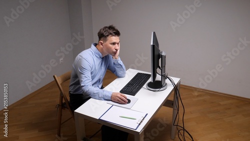 Foto Young man in a blue shirt sitting at a white desk, resting his head on his hand,