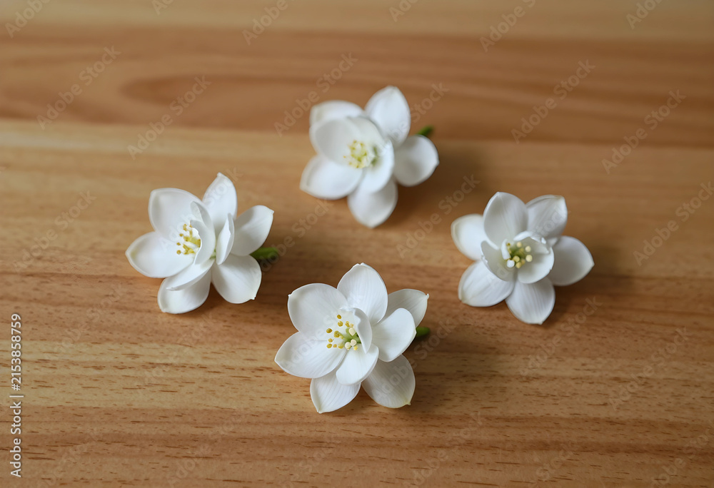 Obraz premium Four delicate white flowers with yellow stamens arranged on a light brown wooden surface, natural beauty and simplicity