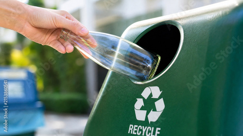 Recycling glass bottle in green bin, hand disposing clear glass into waste container, environmental sustainability and waste management concept