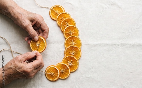 Elderly woman stringing dried orange slices into a rustic garland for handmade Christmas decor