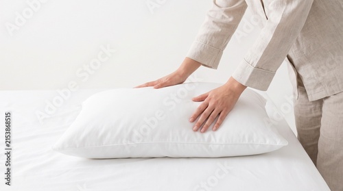 A person's hands smoothing a white pillow on a white bed. The image conveys a sense of comfort, cleanliness, and domesticity