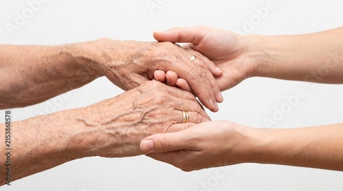 Two hands, one old and wrinkled and the other young and smooth, clasped together in a gesture of support and care. The image evokes feelings of empathy, connection, and the passage of time