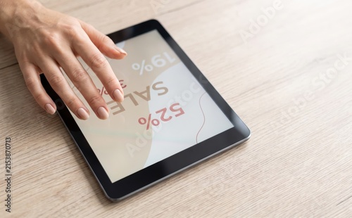 Woman shopping online for sale deals using digital tablet on wooden table