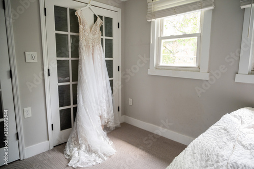 Obraz na płótnie Elegant white lace wedding dress hanging on custom hanger during bridal preparat
