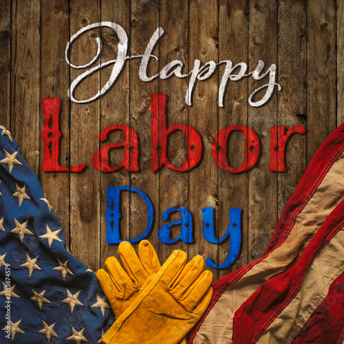 Patriotic Happy Labor Day text with worn work gloves and the USA flag on wooden background. Symbolic of the American labor movement and pride in America's blue collar workers. Celebrate US Labor Day.