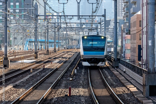 View of a modern commuter train arriving at Ueno Station on the railway tracks surrounded by urban buildings and overhead power lines in Taito City, Tokyo, Japan.