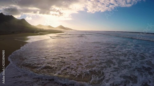 Aerial drone footage of Cofete beach in Fuerteventura at sunset featuring crashing Atlantic ocean waves against dramatic volcanic mountain range in a cinematic travel landscape 4k video