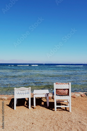 Obraz na plátně Peaceful beach scene with a vintage white wooden chair on golden sand overlooking turquoise sea and blue sky