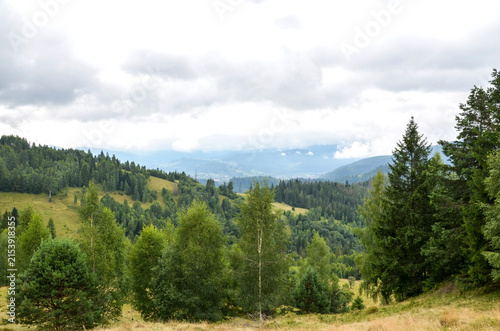 Lush green forest and rolling hills extend into misty mountains under a dramatic cloudy sky, offering a peaceful, rural landscape ideal for hiking, nature photography, outdoor travel and relaxation