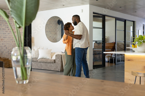 African American couple dancing slowly in open-plan home near beige sofa wearing orange cardigan