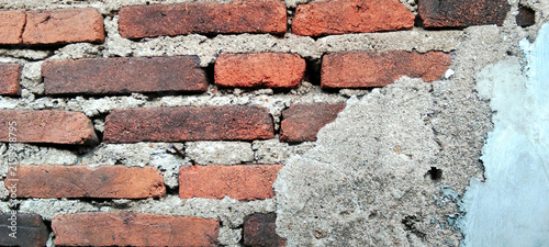 Weathered red brick wall with a partially plastered cement surface.