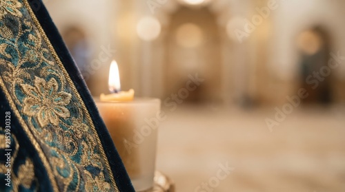 Orthodox church candle burning next to embroidered velvet vestment in a quiet sanctuary representing spirituality, faith, and religious devotion