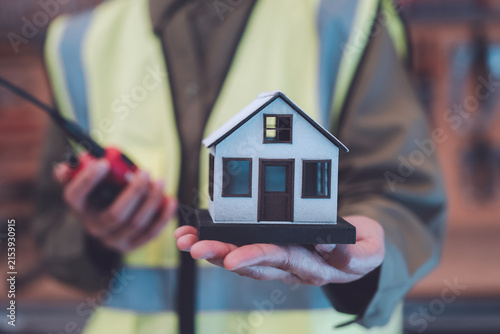 Real estate development construction planning concept industrial worker holding model house and walkie talkie for property management residential housing project and building logistics coordination