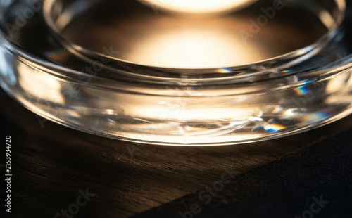 Macro shot of a glowing glass circle refracting warm light on a dark wooden surface, representing abstract modern design and interior lighting concepts