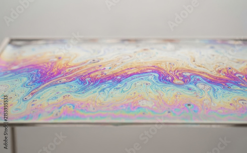 Iridescent soap film table surface abstract macro shot displaying vibrant rainbow interference colors and fluid patterns for modern design backgrounds