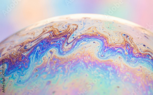 Macro abstract photograph of a colorful soap bubble surface showing iridescent swirling patterns and pastel colors representing physics chemistry and fluid dynamics