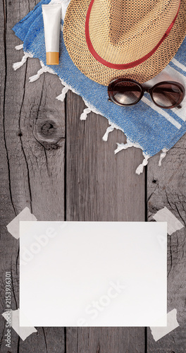 Summer Wallpaper with Straw Hat, Towel, Sunglasses, Protection Cream and White Blank Free Space Paper Sheet with Adhesive Tape on Wooden Surface. File with Clipping Path.